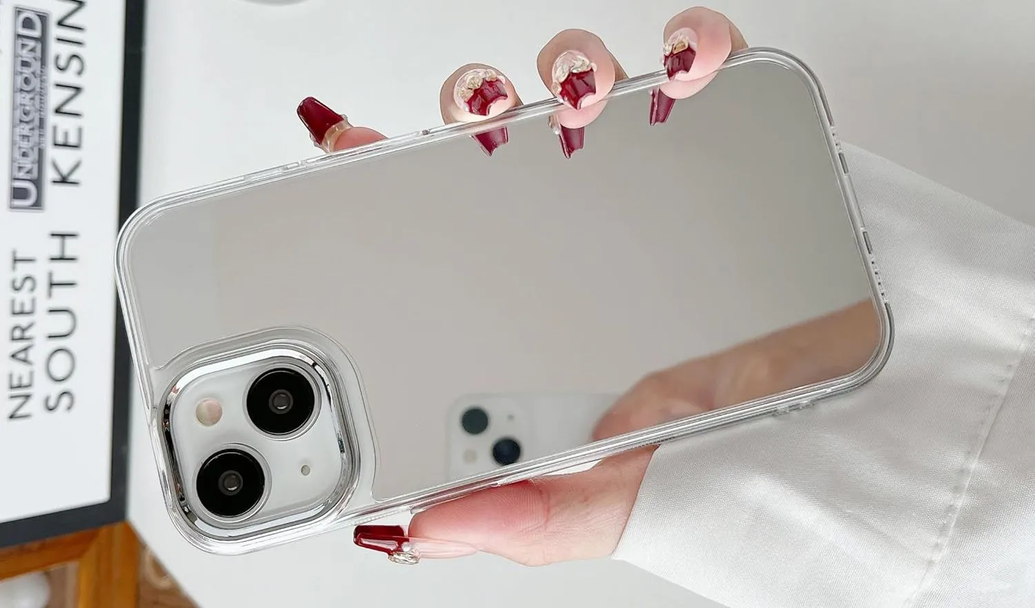 Bàn tay cầm iPhone có ốp lưng tráng gương phản chiếu, giúp kiểm tra ngoại hình nhanh chóng.