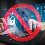 Bàn tay đang gõ laptop với biểu tượng cấm đỏ trên các icon bảo mật, ám chỉ hạn chế quyền truy cập kỹ thuật số.