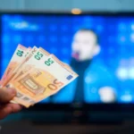 Chiếc tay đang cầm tiền trước màn hình TV thể hiện sự tiết kiệm chi phí khi sở hữu Chromebook
