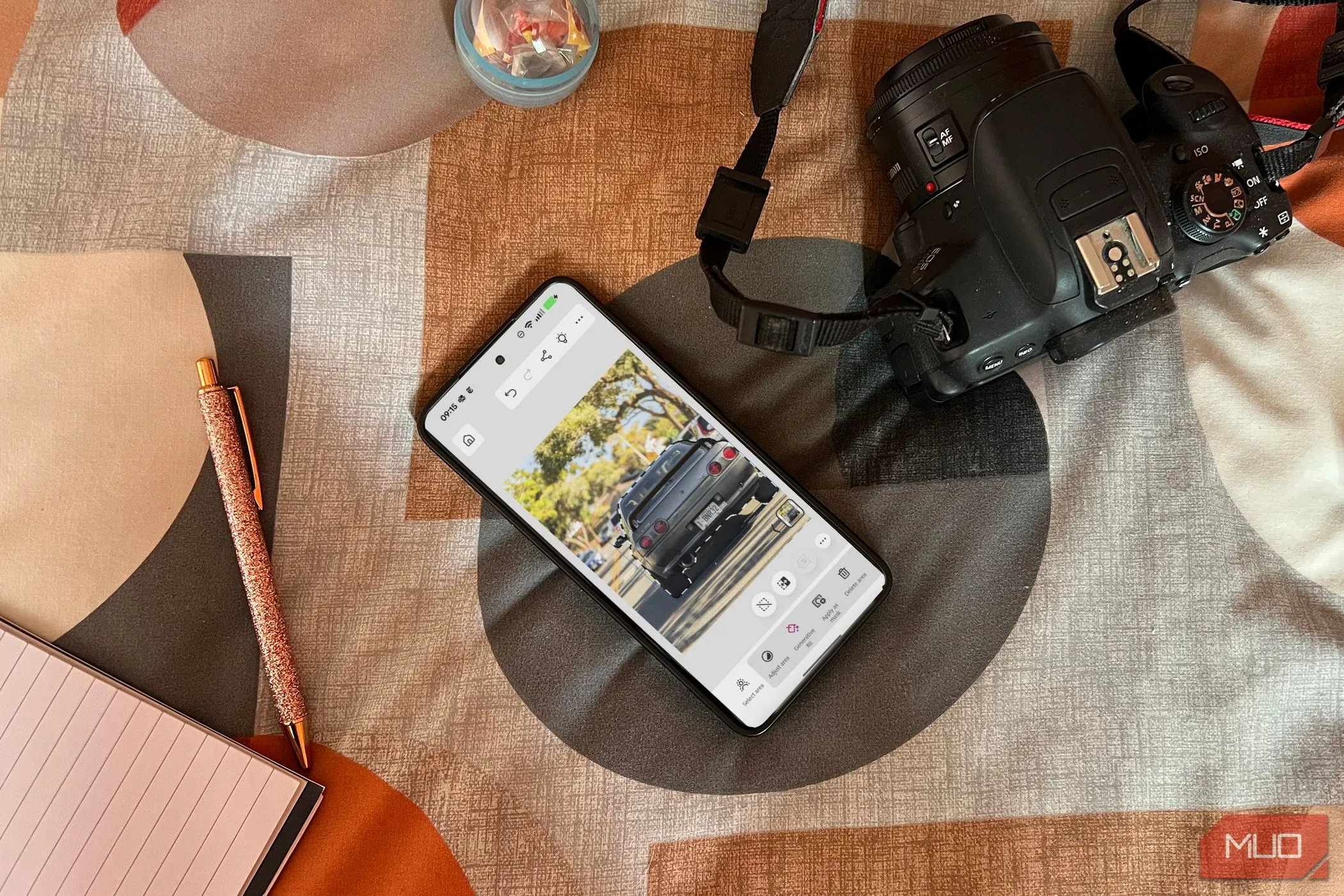 Điện thoại Android hiển thị ứng dụng Photoshop Beta trên giường, cạnh máy ảnh và sổ tay, minh họa khả năng chỉnh sửa ảnh di động.