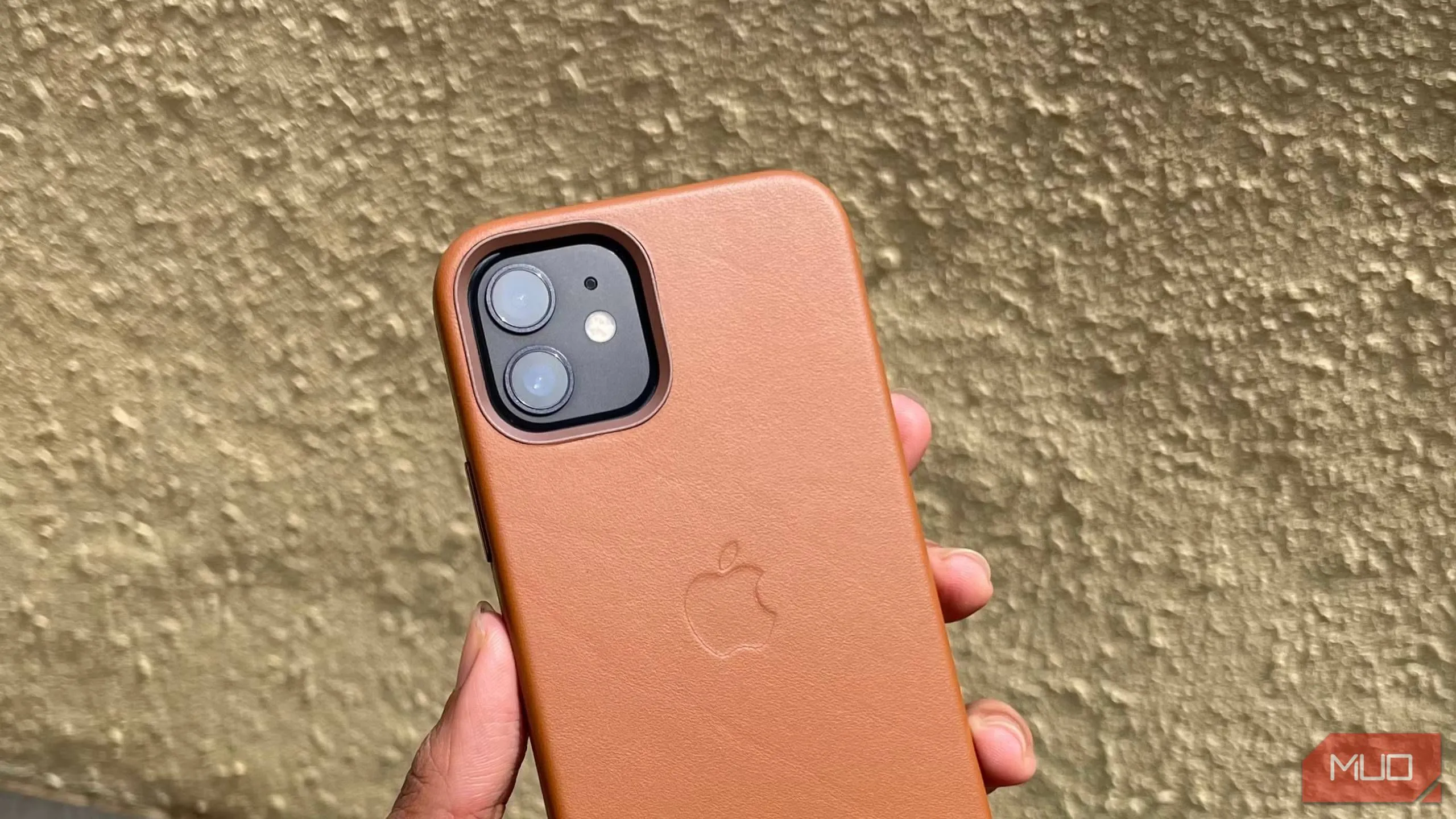 Điện thoại iPhone 12 trong ốp lưng da màu nâu với viền camera nhô cao để bảo vệ ống kính