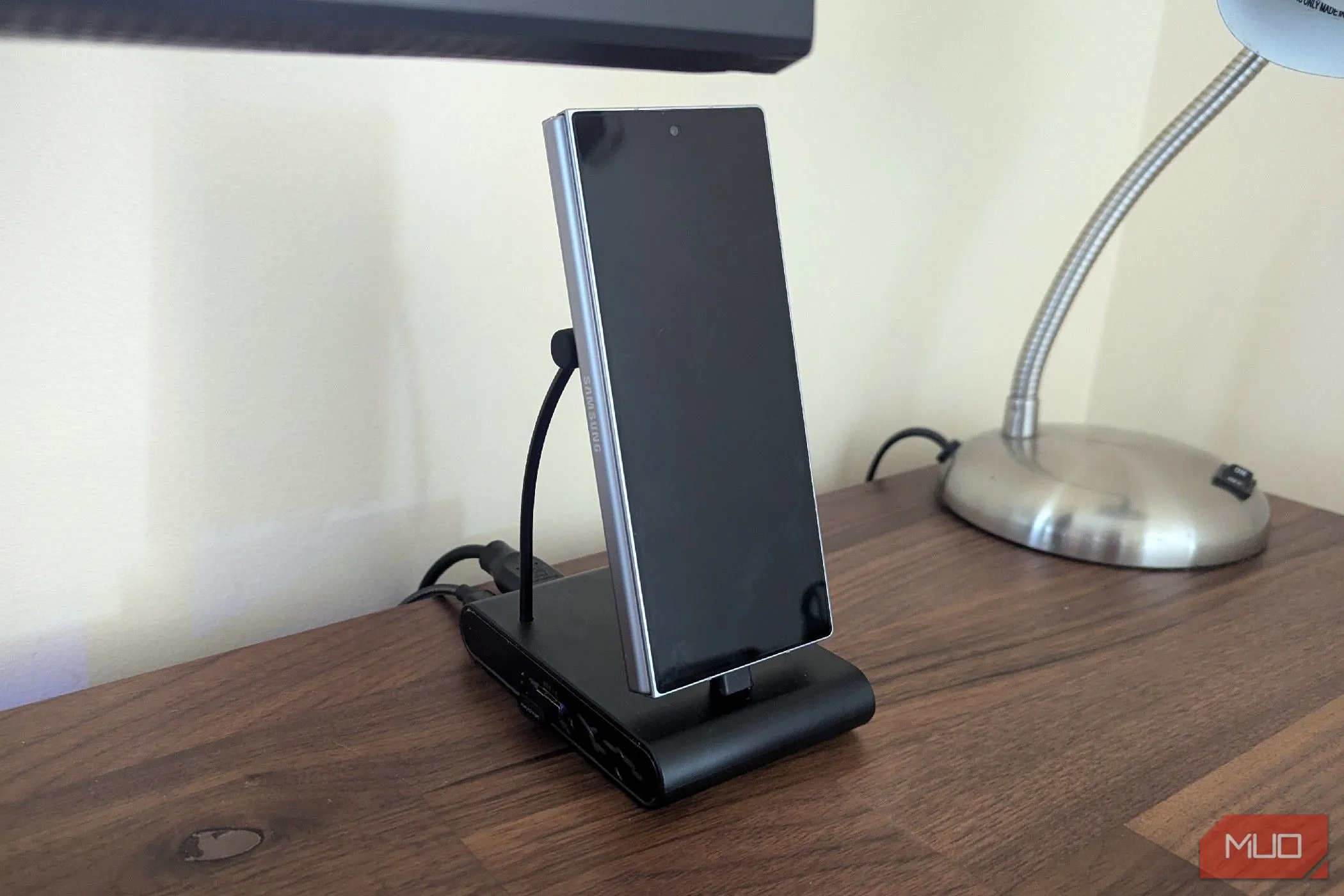 Điện thoại Samsung Galaxy Z Fold 6 đang đặt trên một đế sạc đa năng USB-C thẳng đứng, sẵn sàng cho chế độ máy tính để bàn.