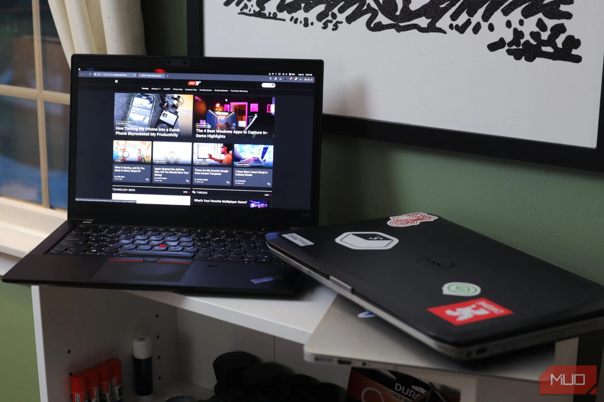 Hai chiếc laptop đặt trên kệ trắng, một chiếc mở ra trang MakeUseOf.