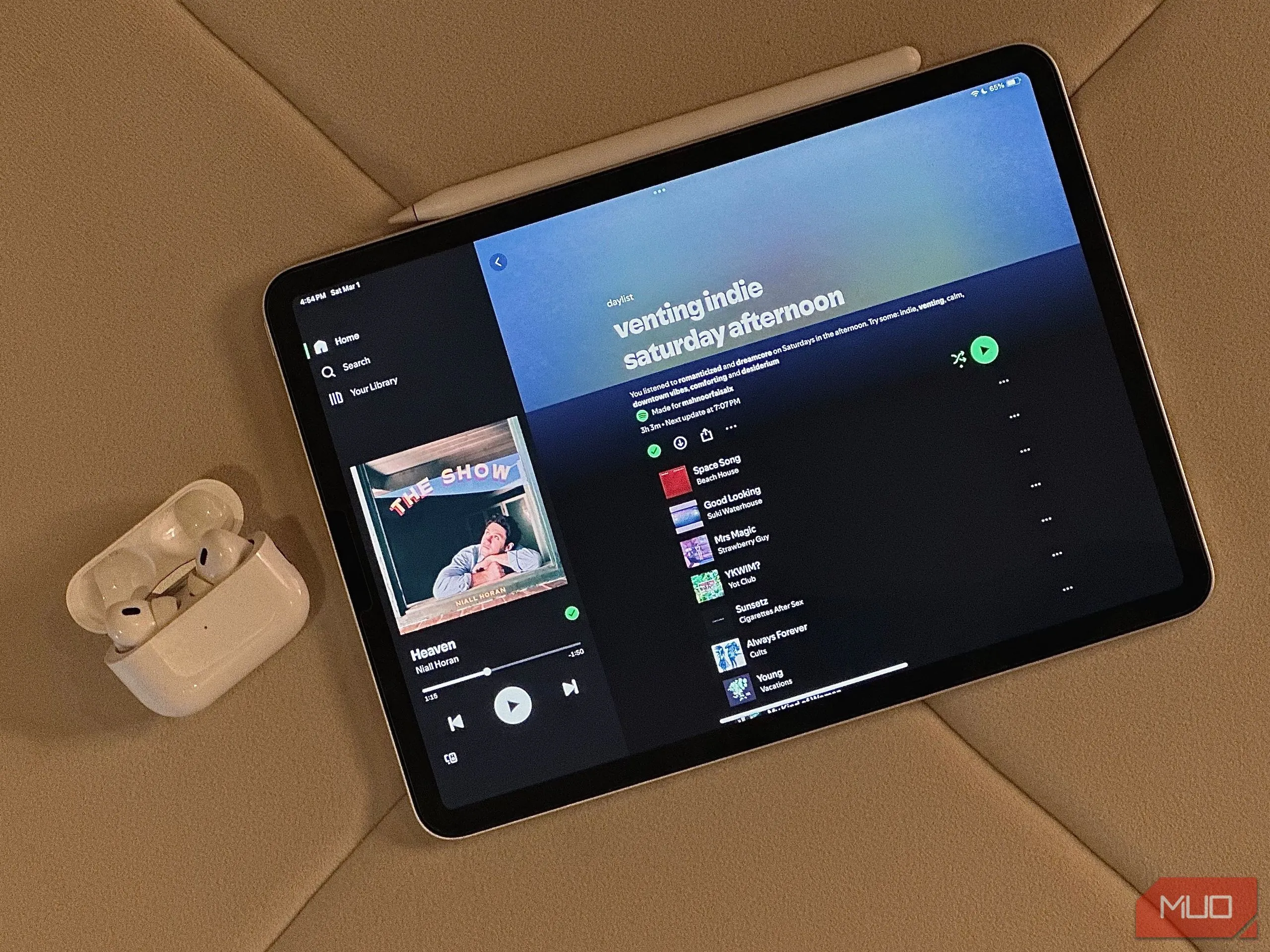 Hình ảnh minh họa chiếc iPad hiển thị ứng dụng Daylist, đặt cạnh hộp đựng tai nghe Apple AirPods trước khi chỉnh sửa.
