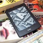Kindle Paperwhite đặt trên chồng sách giấy bên cửa sổ