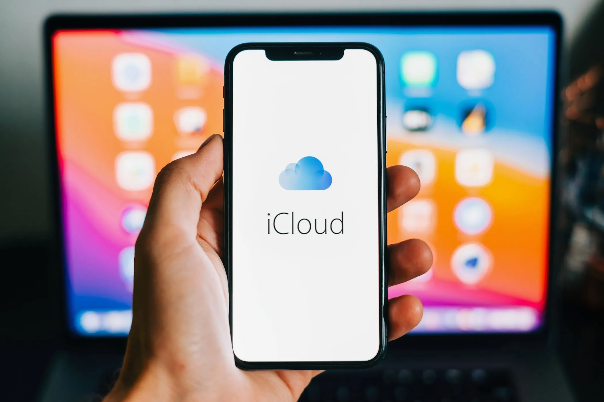 Logo iCloud xuất hiện trên iPhone với MacBook phía sau, thể hiện sự tích hợp hệ sinh thái Apple