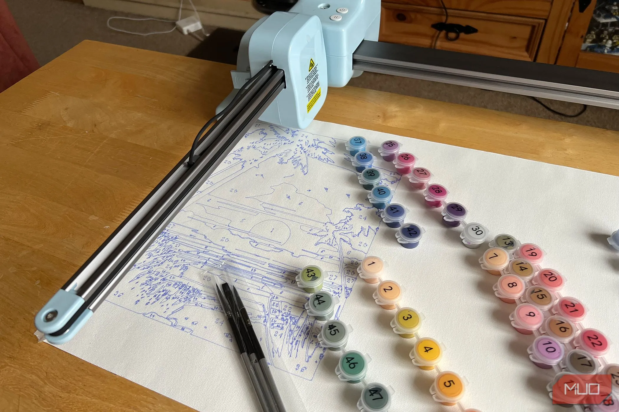 Máy LOKLiK iPaint đang vẽ một bức tranh hoàng hôn, bên cạnh là các hộp màu được đánh số