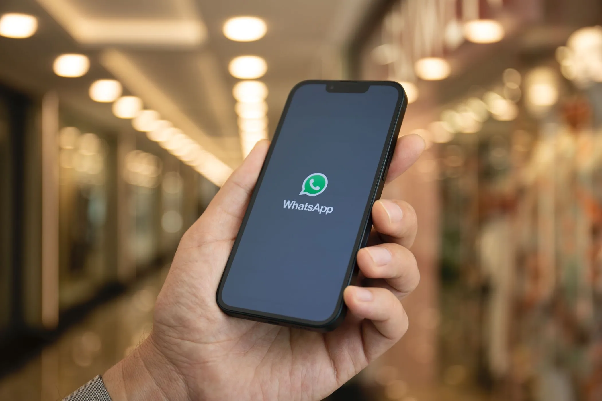 Một bàn tay đang cầm điện thoại thông minh hiển thị logo WhatsApp và tính năng phiên âm tin nhắn thoại