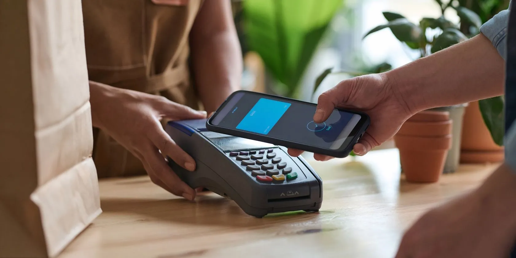 Một người đàn ông dùng mặt lưng điện thoại để thanh toán không tiếp xúc qua NFC tại quầy thu ngân.