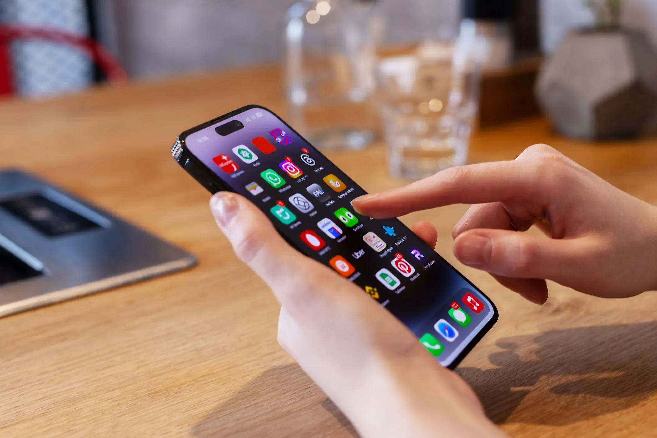 Một người đang sử dụng iPhone trên bàn với cốc nước phía sau.