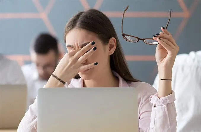 Một phụ nữ đang dụi mắt, biểu thị tình trạng mỏi mắt do sử dụng thiết bị điện tử