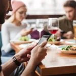 Người đàn ông đang dùng điện thoại trong quán cà phê cùng bạn bè