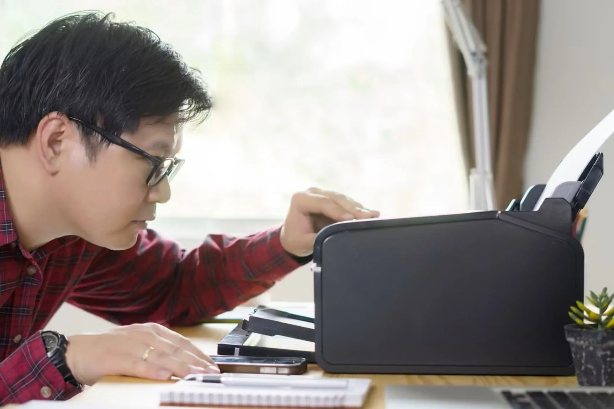 Người đàn ông đang nhìn vào máy in trên bàn, biểu thị vấn đề tương thích của Chromebook với một số thiết bị ngoại vi.
