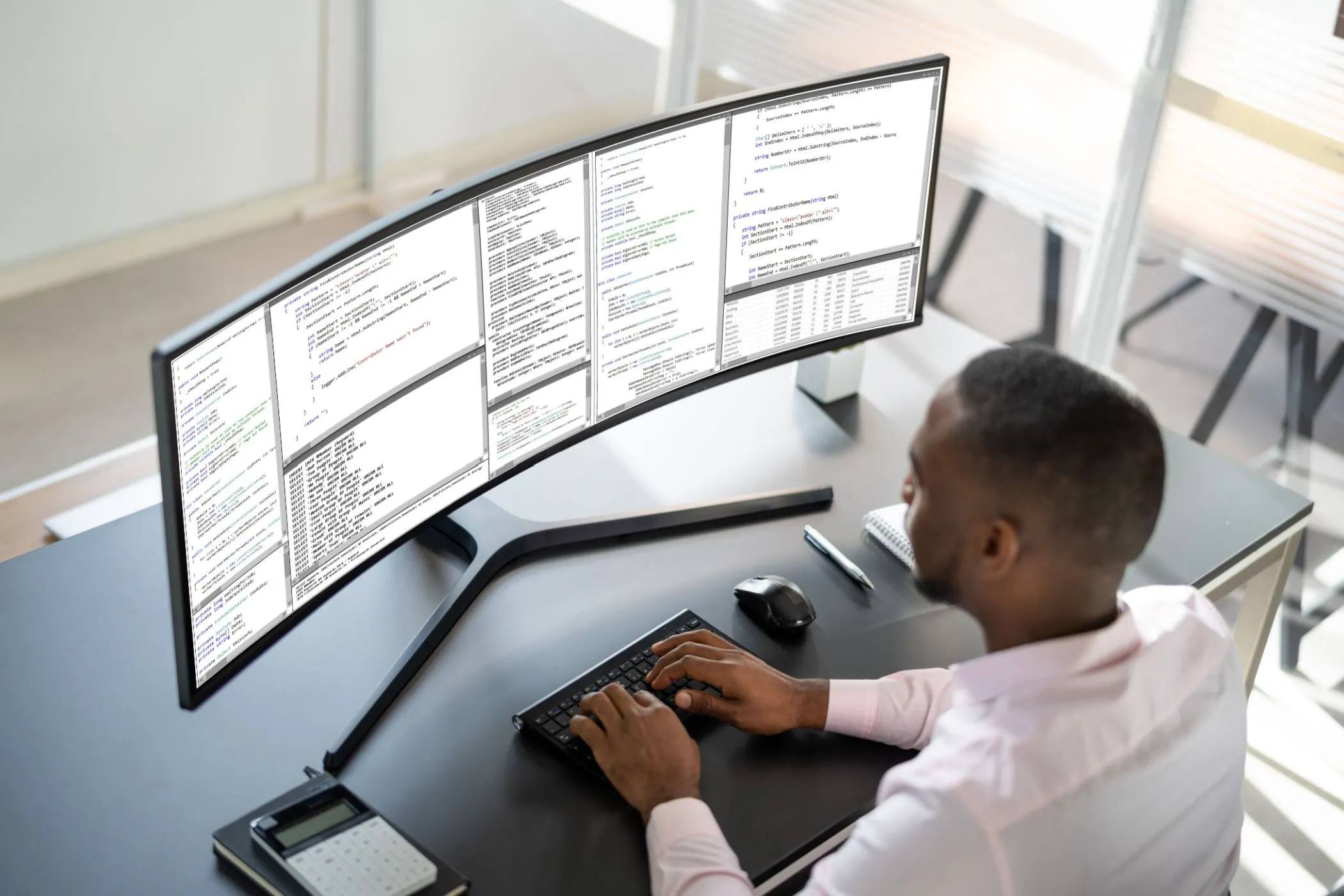 Người đàn ông làm việc với màn hình siêu rộng (ultrawide) trên bàn làm việc, thể hiện xu hướng màn hình lớn trong bối cảnh thiếu màn hình 4K nhỏ.