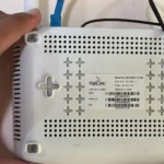 Người dùng đang cầm bộ định tuyến Wi-Fi để kiểm tra thông tin đăng nhập mặc định phía sau thiết bị.