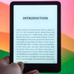 Thiết bị Amazon Kindle Paperwhite Signature Edition trên bàn, cạnh màn hình máy tính hiển thị nội dung đọc sách điện tử.