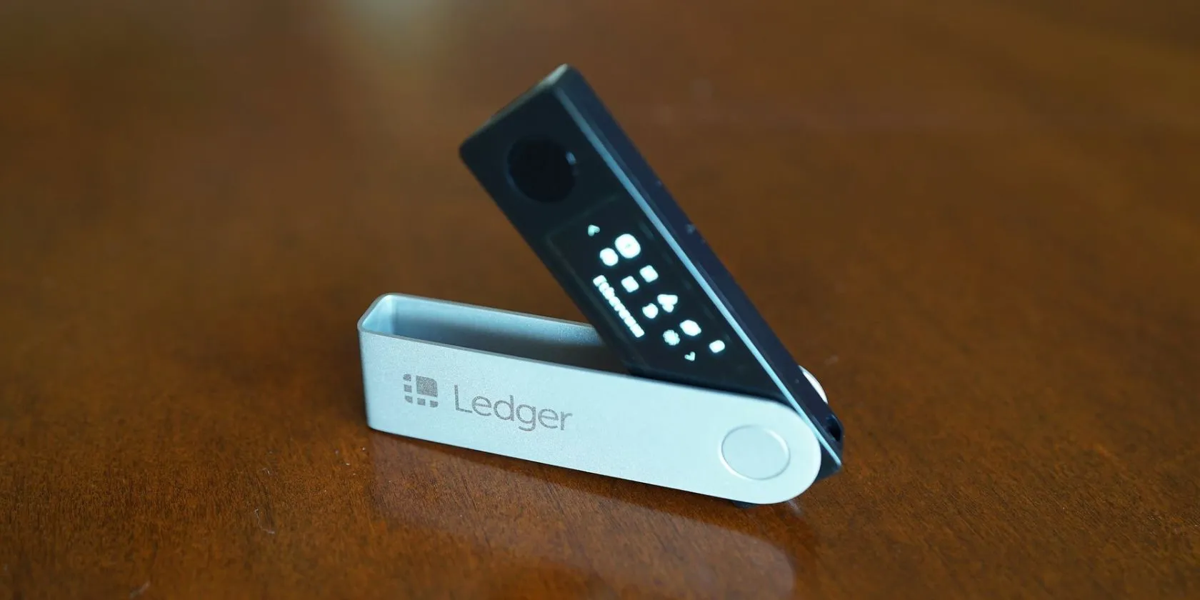 Thiết bị ví lạnh Ledger Nano X màu đen đặt trên bề mặt gỗ, đại diện cho phương thức lưu trữ tiền mã hóa an toàn.